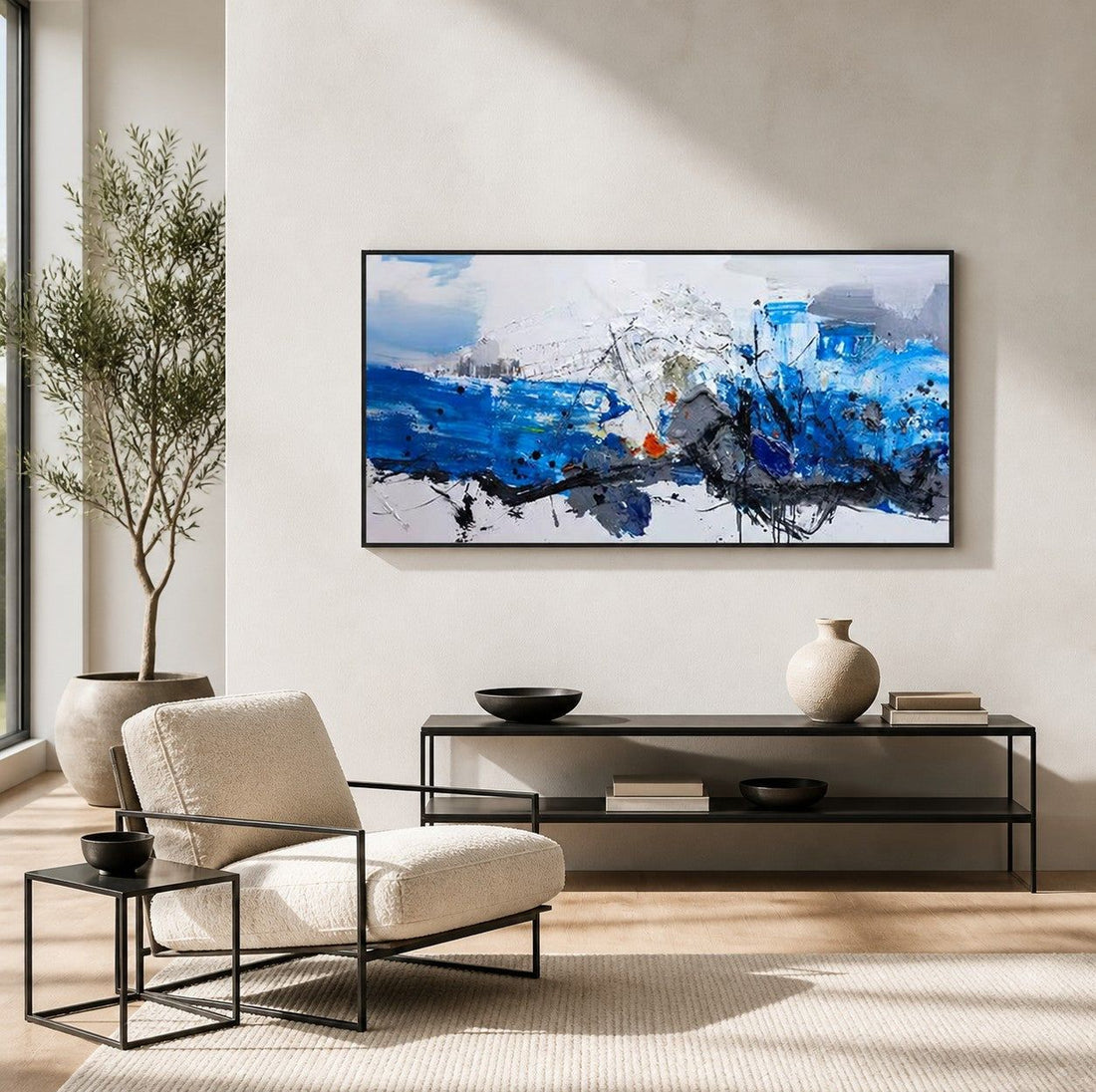 Large vivid blue abstract painting above a boucle armchair in a bright, white-walled contemporary living room with an olive tree