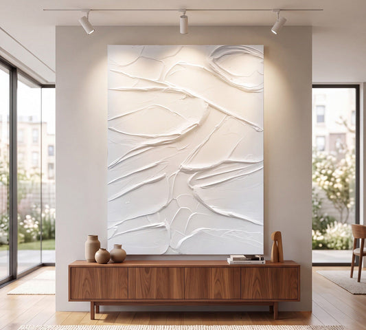 Sculpted Serenity, a raised white plaster-relief abstract painting in a floating frame, hung above a low console in a quiet neutral living room with linen upholstery